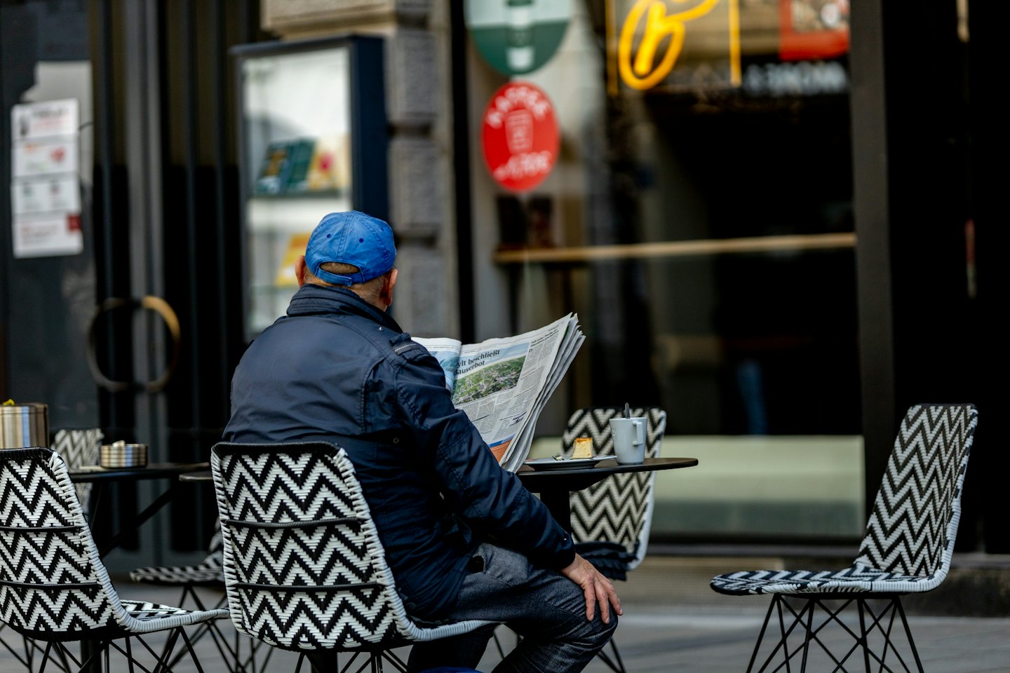 Persona legge il giornale a un tavolino del bar con caffè e torta.